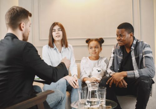 Family counseling session at home with therapist. Pshycologist showing pictures of emotions to a girL.African American father and European mother.